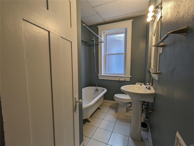 bathroom featuring tile patterned flooring, a paneled ceiling, toilet, and a tub