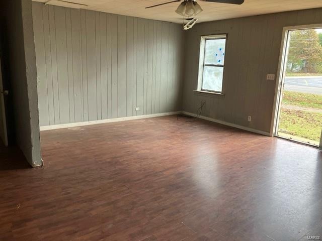 unfurnished room with wooden walls, plenty of natural light, ceiling fan, and dark wood-type flooring