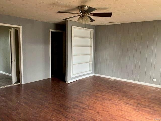 unfurnished room with dark hardwood / wood-style flooring, built in features, ceiling fan, and wood walls