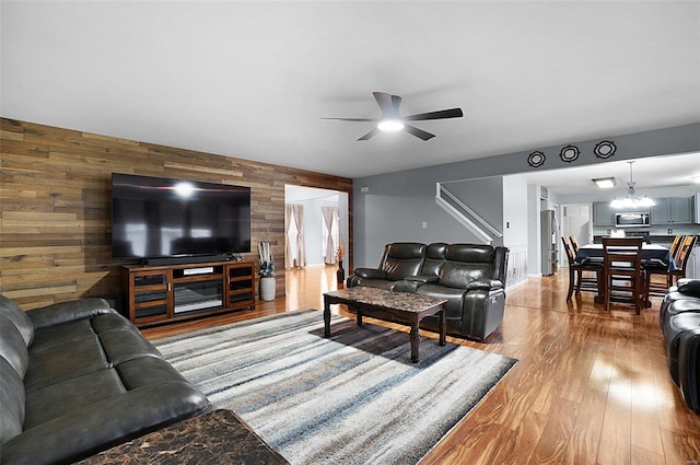 living room with hardwood / wood-style flooring, ceiling fan with notable chandelier, and wood walls