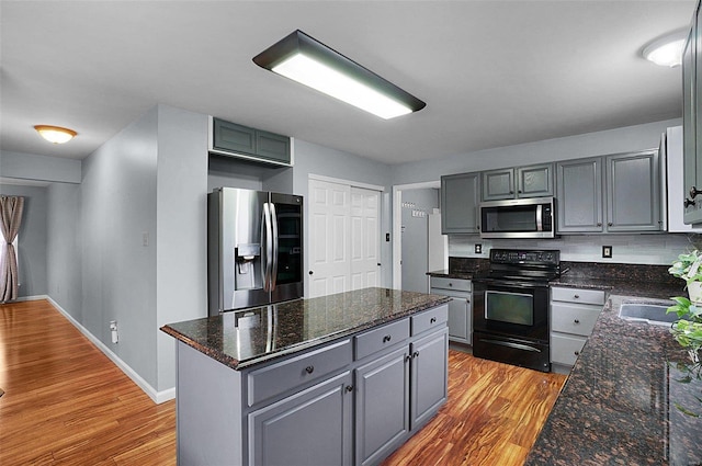 kitchen with sink, light hardwood / wood-style flooring, dark stone countertops, a kitchen island, and appliances with stainless steel finishes