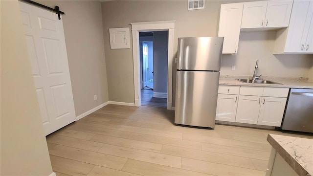 kitchen featuring appliances with stainless steel finishes, sink, a barn door, light hardwood / wood-style flooring, and white cabinetry