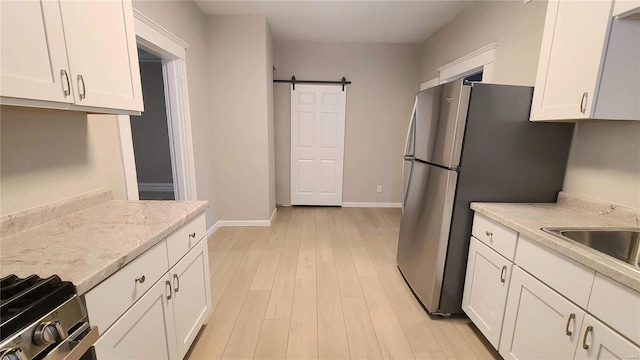 kitchen featuring light wood-type flooring, a barn door, white cabinetry, and light stone countertops