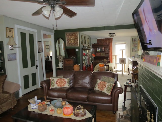 living room with ceiling fan, a fireplace, and dark wood-type flooring