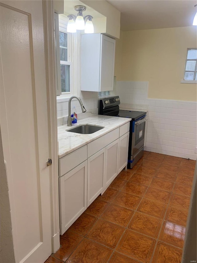 kitchen with stainless steel electric stove, white cabinetry, sink, and light stone counters