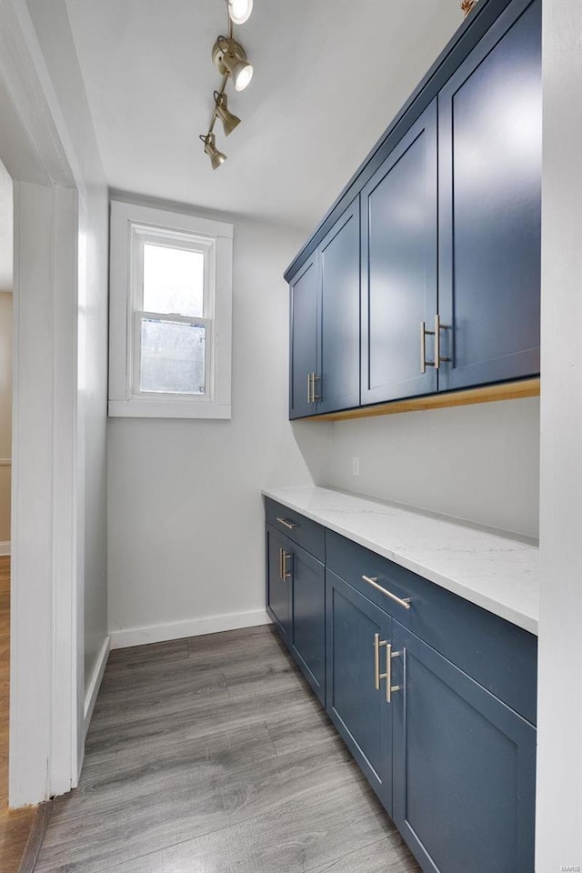 bar with light stone countertops, blue cabinetry, and light hardwood / wood-style flooring