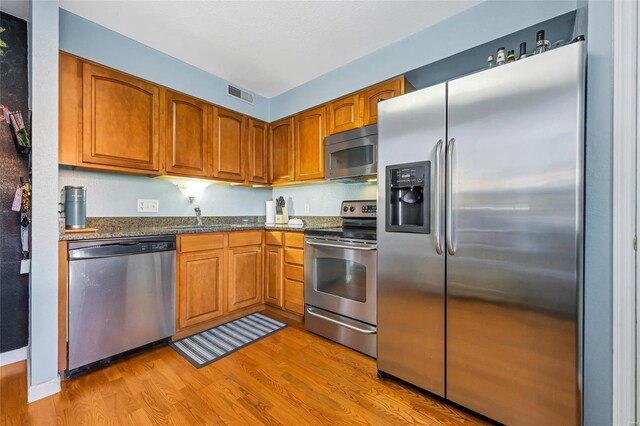 kitchen featuring light hardwood / wood-style floors, dark stone countertops, sink, and appliances with stainless steel finishes