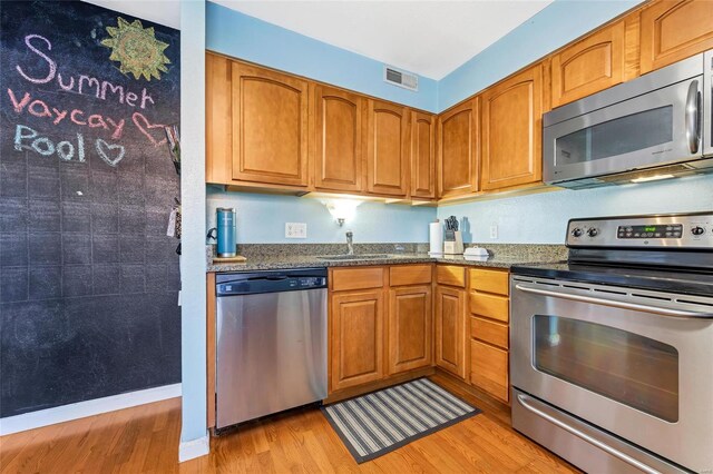 kitchen with dark stone counters, sink, stainless steel appliances, and light wood-type flooring