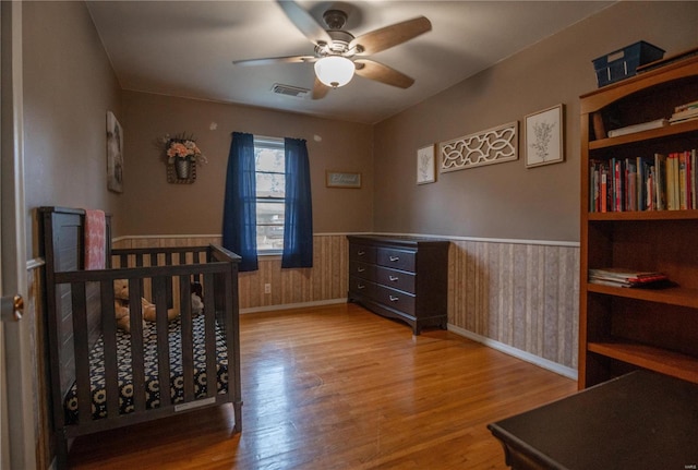 bedroom with ceiling fan, light hardwood / wood-style floors, wooden walls, and a nursery area