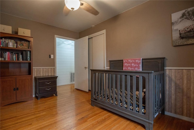 bedroom with ceiling fan, light hardwood / wood-style floors, wooden walls, and a closet