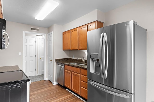 kitchen featuring sink, light hardwood / wood-style flooring, dark stone countertops, a textured ceiling, and appliances with stainless steel finishes