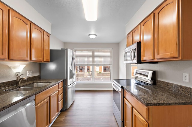 kitchen with a textured ceiling, stainless steel appliances, dark wood-type flooring, sink, and dark stone countertops