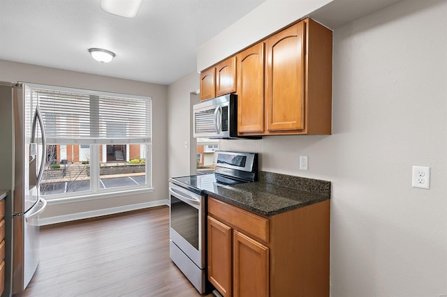 kitchen with appliances with stainless steel finishes, light hardwood / wood-style flooring, and dark stone countertops