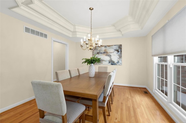 dining area featuring a raised ceiling, light hardwood / wood-style floors, and a chandelier