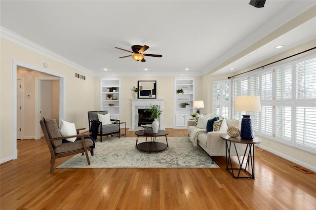 living room with ornamental molding, ceiling fan, built in features, and light hardwood / wood-style flooring