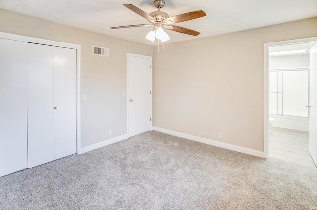 unfurnished bedroom featuring a closet, light colored carpet, ceiling fan, and ensuite bathroom