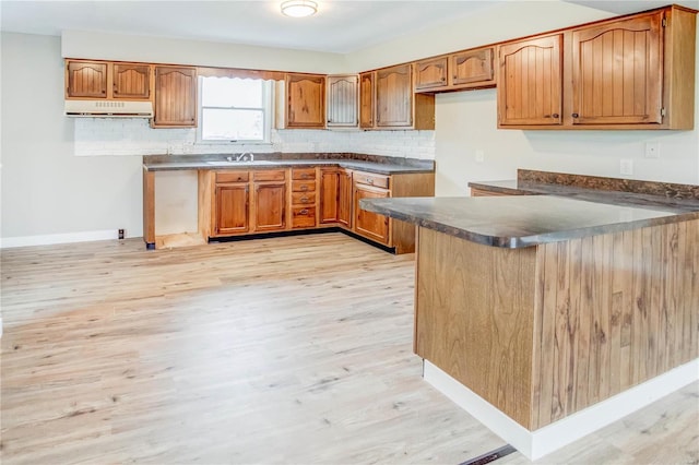 kitchen with kitchen peninsula, decorative backsplash, light hardwood / wood-style flooring, and sink