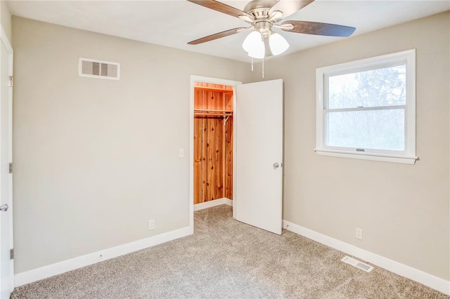 unfurnished bedroom featuring a walk in closet, a closet, light colored carpet, and ceiling fan