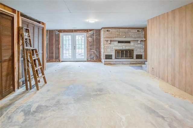 unfurnished living room featuring concrete flooring, a fireplace, wooden walls, and french doors