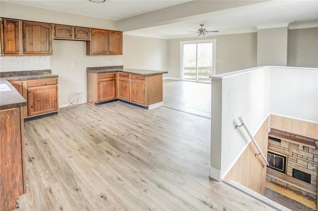 kitchen with backsplash, a stone fireplace, ceiling fan, light wood-type flooring, and kitchen peninsula