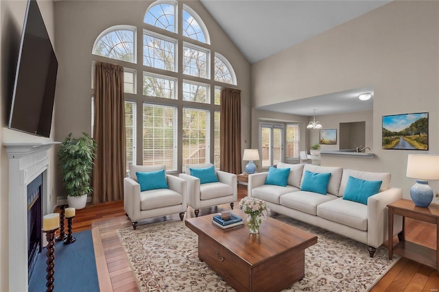 living room featuring a wealth of natural light, light hardwood / wood-style flooring, high vaulted ceiling, and a chandelier