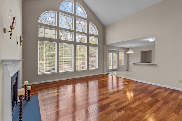 unfurnished living room with hardwood / wood-style flooring, high vaulted ceiling, and an inviting chandelier