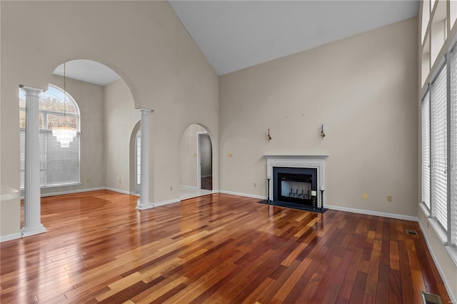 unfurnished living room featuring hardwood / wood-style floors, high vaulted ceiling, and decorative columns