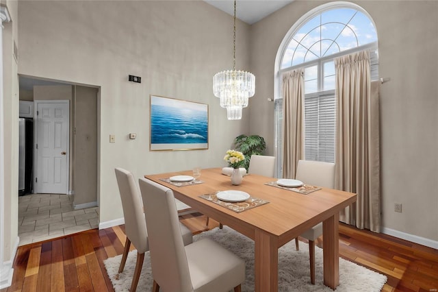 dining space with wood-type flooring, a towering ceiling, and a chandelier