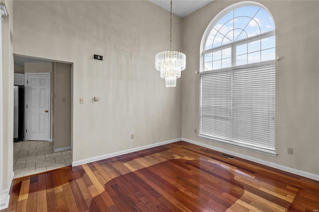 spare room featuring hardwood / wood-style floors, a high ceiling, and a chandelier