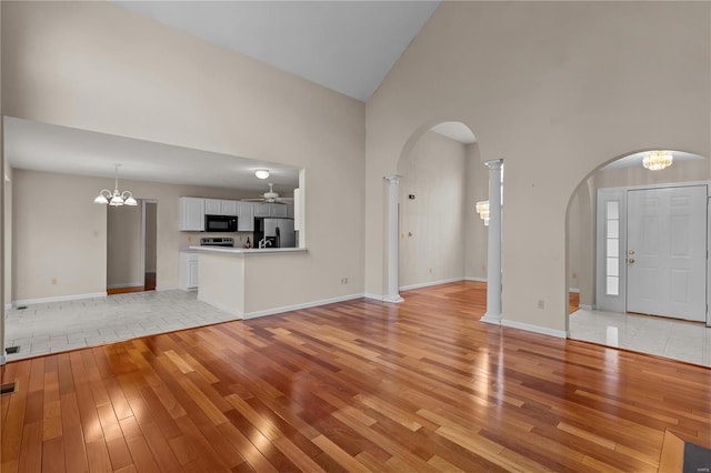 unfurnished living room featuring high vaulted ceiling, light hardwood / wood-style floors, and ceiling fan with notable chandelier