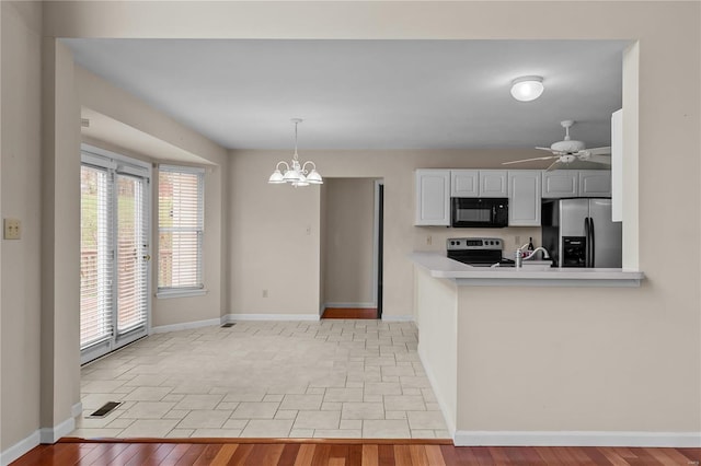 kitchen featuring pendant lighting, ceiling fan with notable chandelier, light hardwood / wood-style flooring, kitchen peninsula, and stainless steel appliances