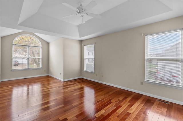 empty room featuring ceiling fan, wood-type flooring, and a tray ceiling