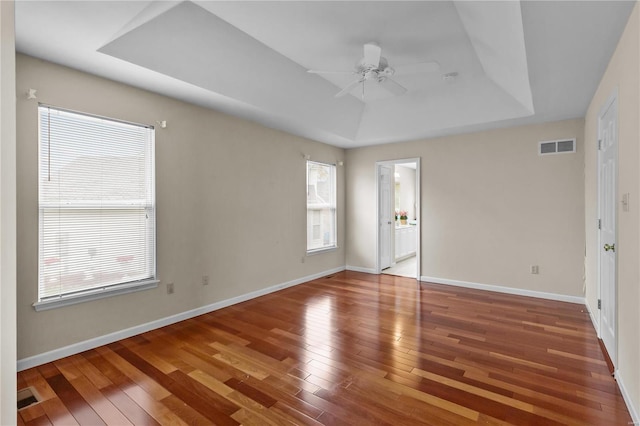 unfurnished room with hardwood / wood-style flooring, plenty of natural light, ceiling fan, and a raised ceiling