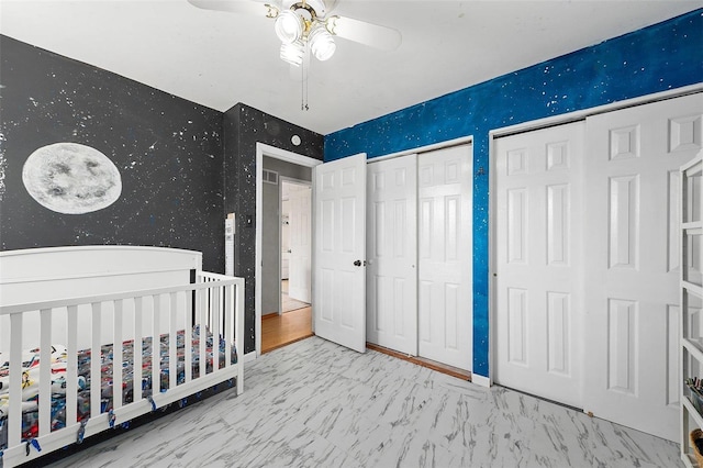 unfurnished bedroom with baseboards, marble finish floor, a nursery area, two closets, and wallpapered walls