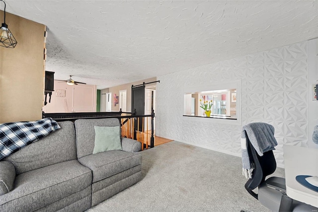 carpeted living area with a ceiling fan, a textured ceiling, and a barn door