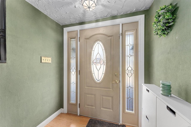 foyer entrance featuring a textured wall, light wood-style flooring, and baseboards