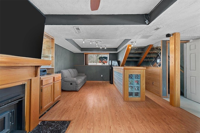 living room with light wood-style floors, visible vents, a textured ceiling, and rail lighting