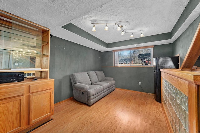 sitting room with light wood finished floors, a raised ceiling, rail lighting, a textured ceiling, and baseboards