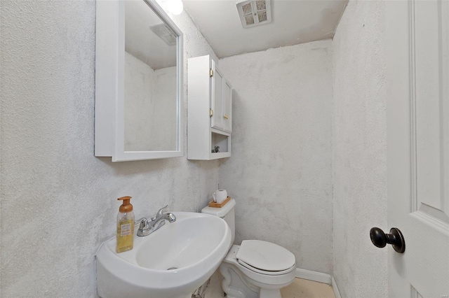 bathroom with toilet, a textured wall, a sink, and visible vents