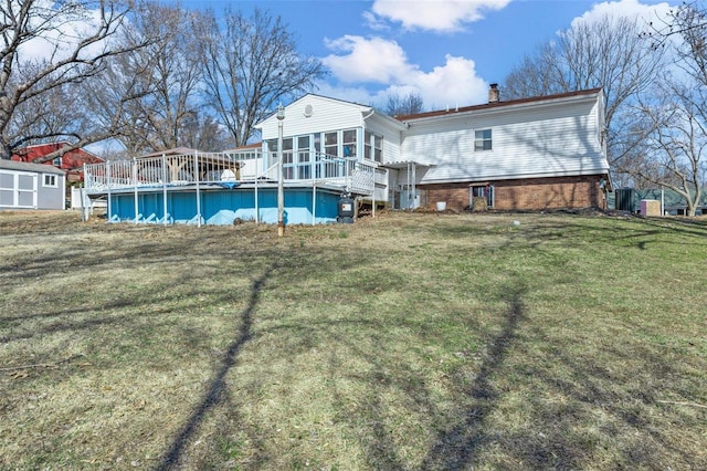 back of property with brick siding, a sunroom, a lawn, an outdoor pool, and a chimney