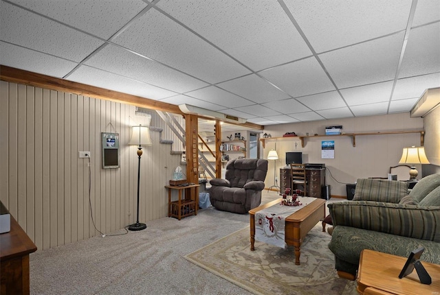 living room with carpet flooring, a drop ceiling, and wood walls