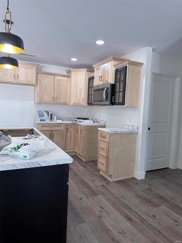 kitchen featuring glass insert cabinets, stainless steel microwave, hanging light fixtures, light countertops, and light brown cabinets