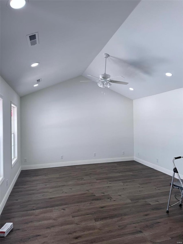 empty room with dark wood-style flooring, visible vents, a ceiling fan, vaulted ceiling, and baseboards