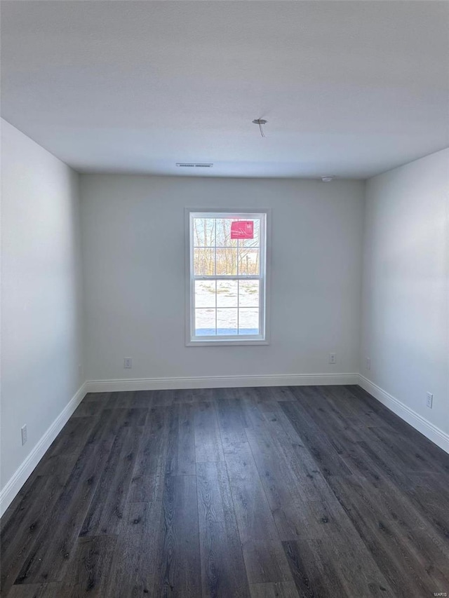 empty room with baseboards, visible vents, and dark wood-type flooring