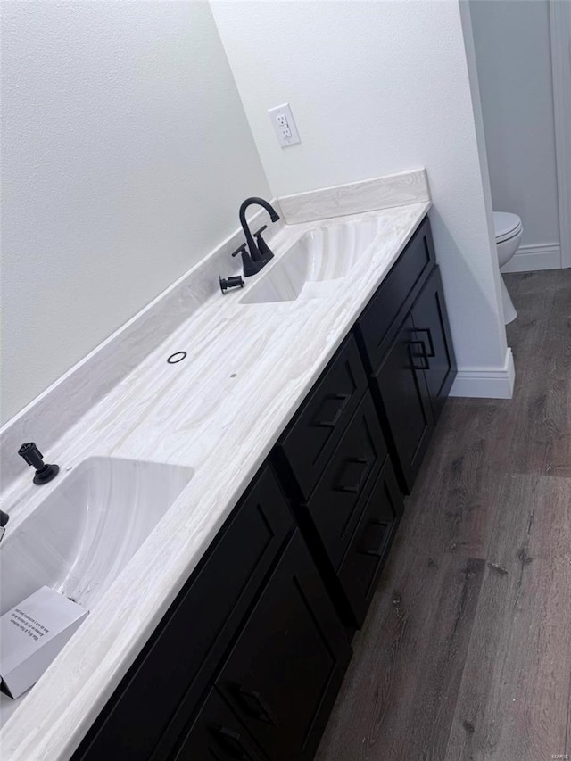 bathroom featuring double vanity, a sink, toilet, and wood finished floors