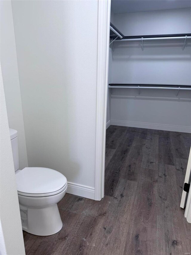 bathroom with toilet, a spacious closet, baseboards, and wood finished floors