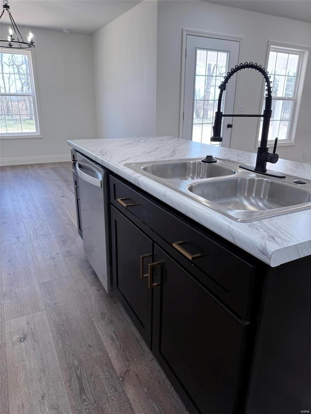 kitchen featuring dishwasher, dark cabinets, a kitchen island with sink, light wood-type flooring, and a sink