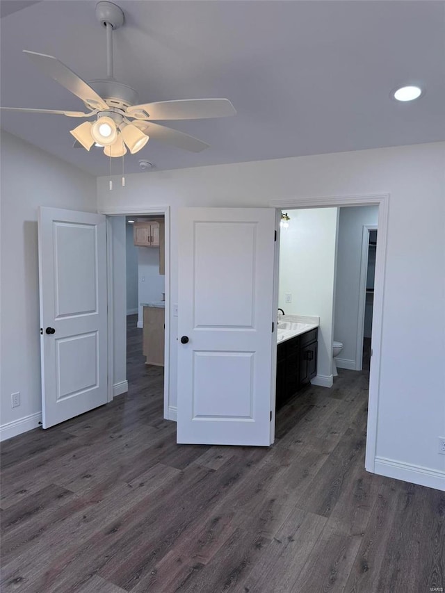 unfurnished bedroom featuring a sink, baseboards, dark wood finished floors, and connected bathroom