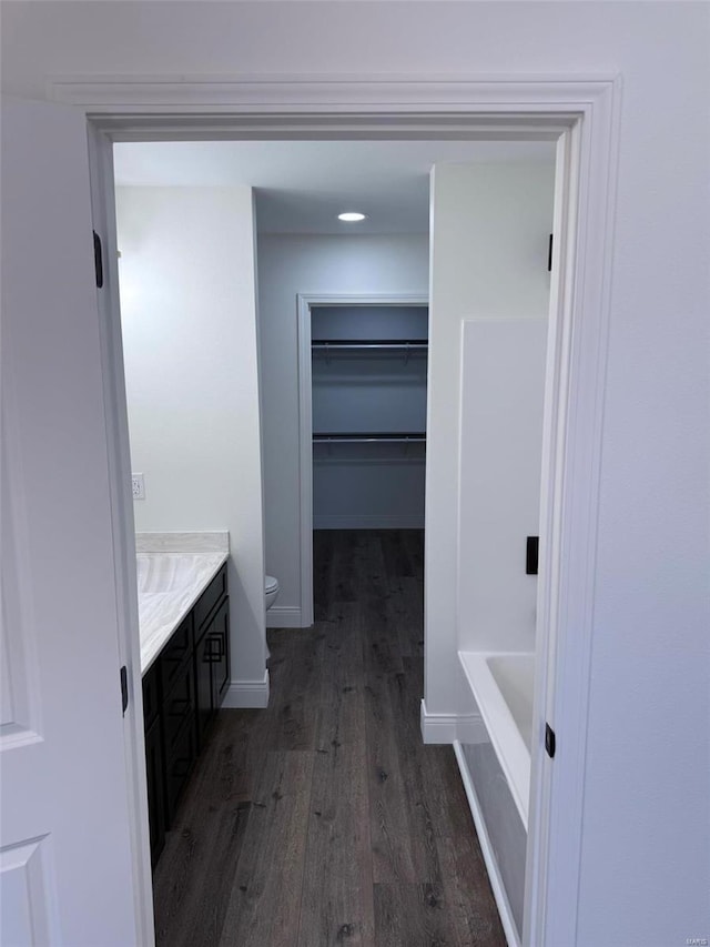 full bath featuring toilet, wood finished floors, vanity, baseboards, and a walk in closet