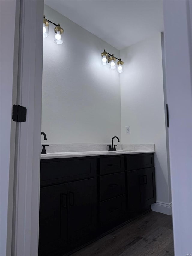 full bathroom featuring double vanity, baseboards, a sink, and wood finished floors